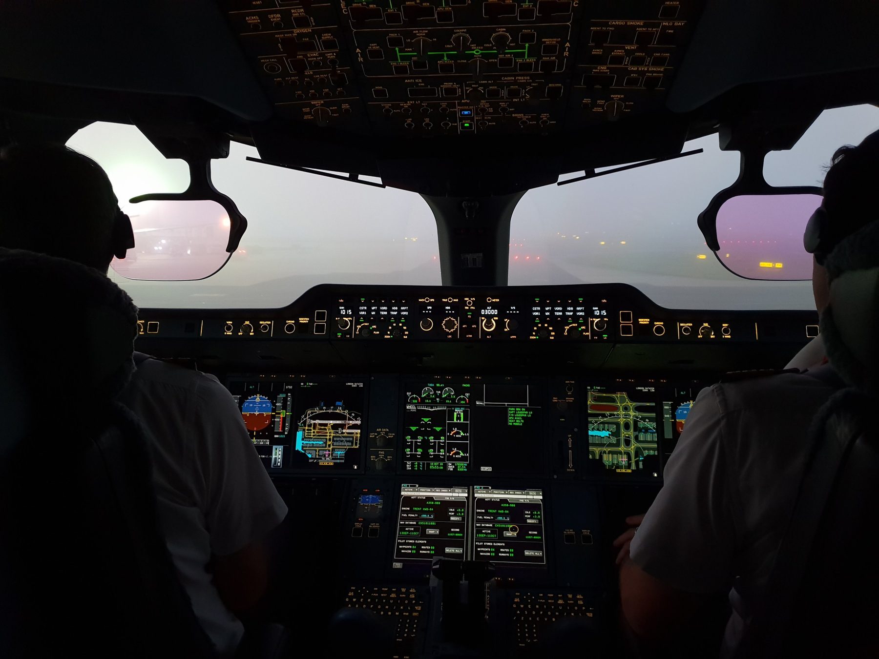 A pilot at the controls on a foggy morning, the flight deck lit by the instrument displays